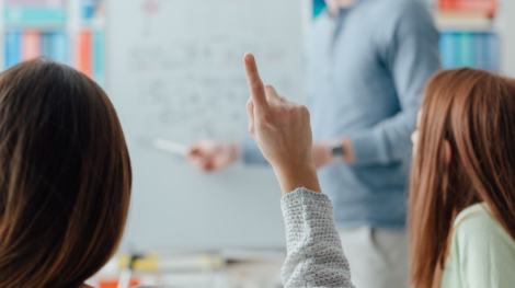 Young researcher giving a lecture to a group of students, a student is raising her hand and asking a question