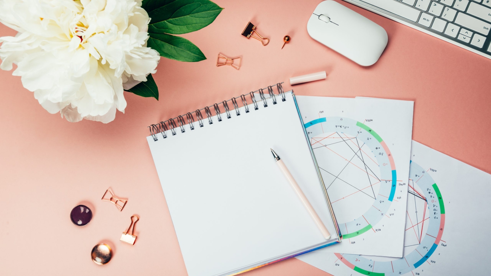 Open Notebook for writing ideas and astrological birth natal chart laying on pink background. Computer keyboard and mouse nearby. Idea of Astrological Consultation. Flat lay in girly style