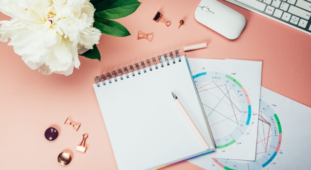 Open Notebook for writing ideas and astrological birth natal chart laying on pink background. Computer keyboard and mouse nearby. Idea of Astrological Consultation. Flat lay in girly style