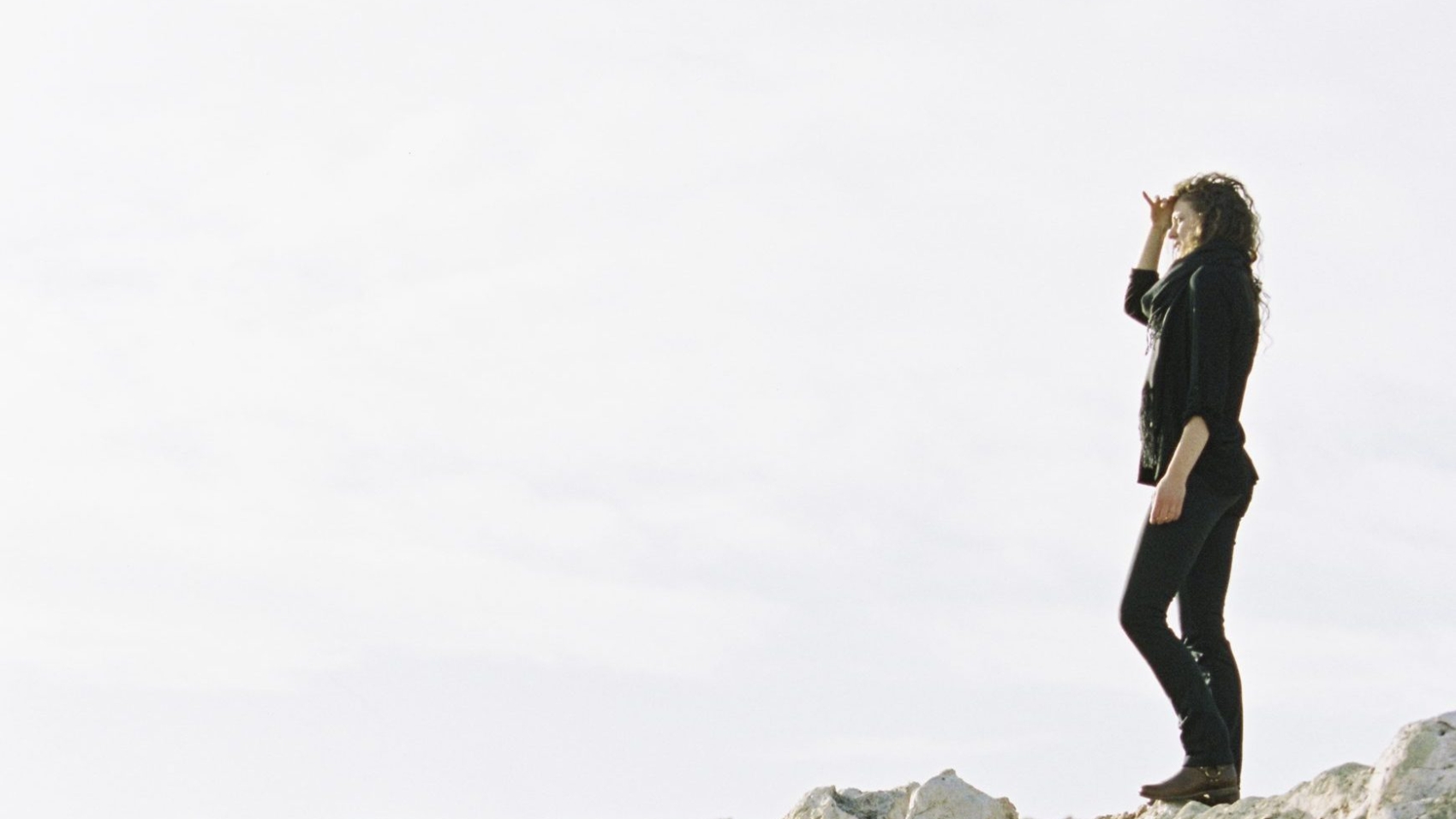 A woman standing on a rock shielding her eyes from the sun with her hand.