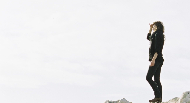 A woman standing on a rock shielding her eyes from the sun with her hand.