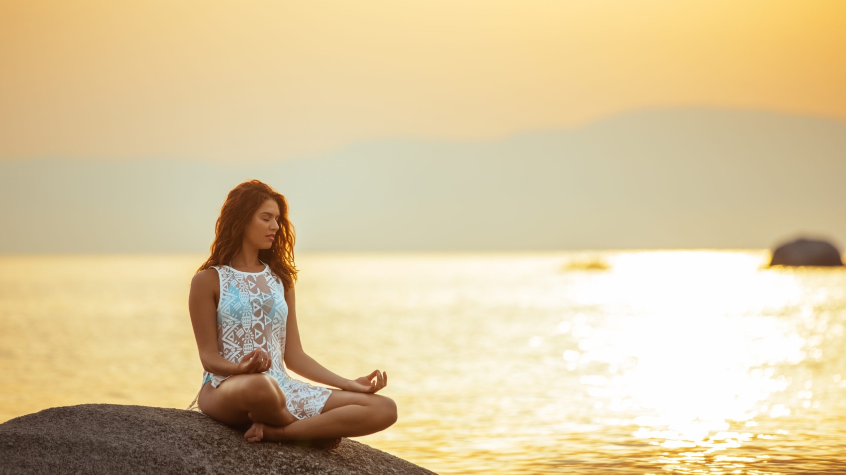 Full length portrait of a young woman meditating by the ocean.