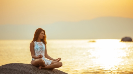 Full length portrait of a young woman meditating by the ocean.
