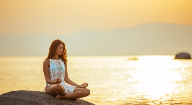 Full length portrait of a young woman meditating by the ocean.