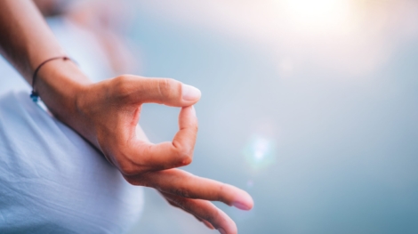 Close up image of woman’s hands in lotus position by the lake