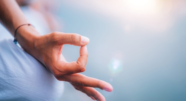 Close up image of woman’s hands in lotus position by the lake