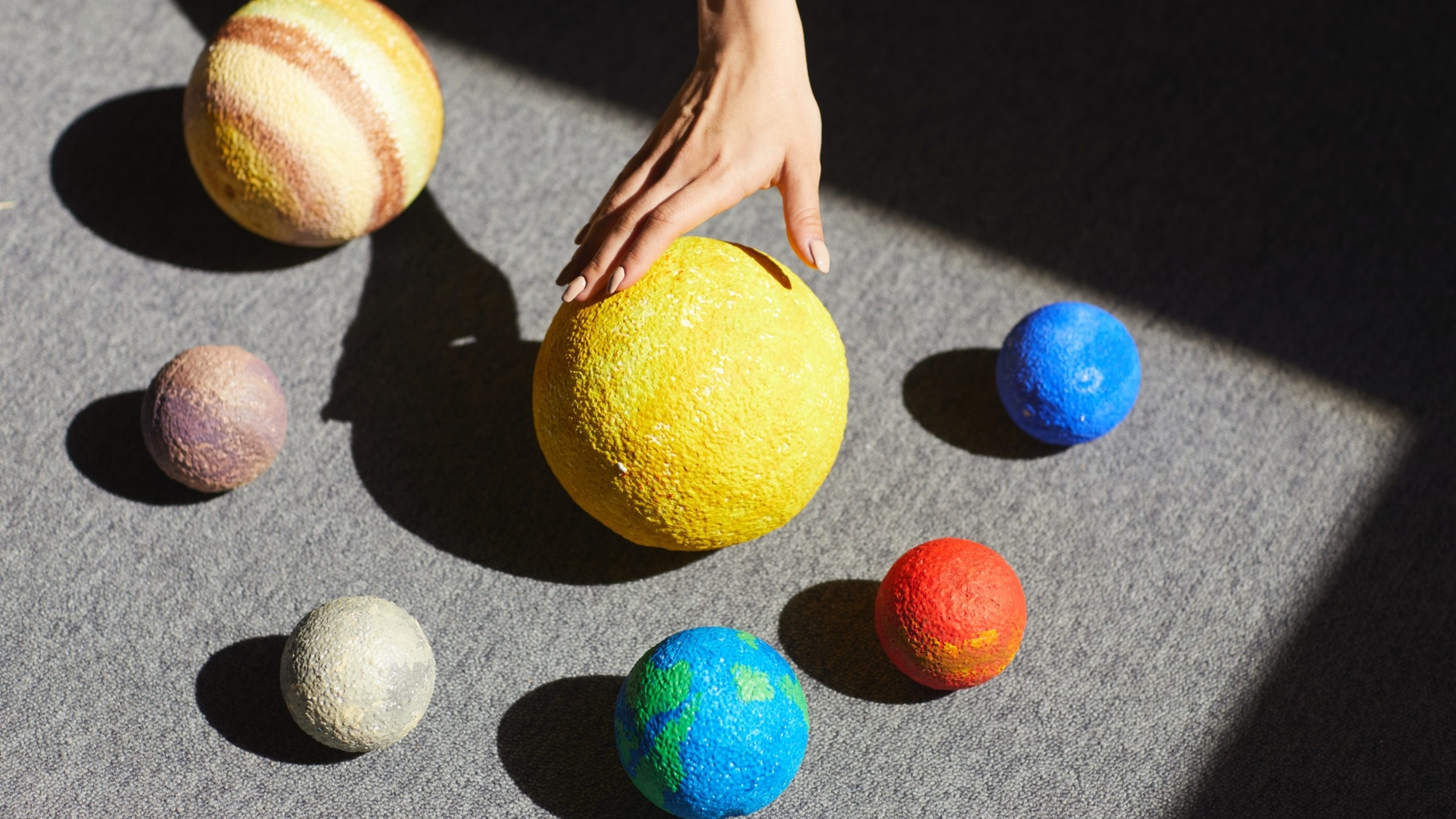 Above view of unrecognizable woman placing planet models according to solar system in light on floor