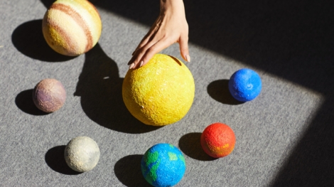 Above view of unrecognizable woman placing planet models according to solar system in light on floor