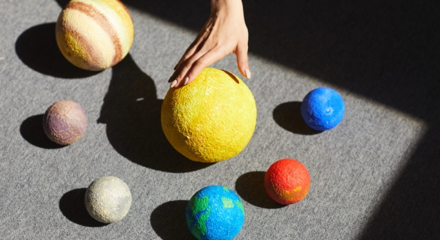 Above view of unrecognizable woman placing planet models according to solar system in light on floor