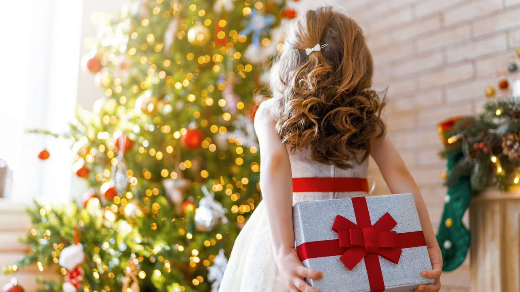 Merry Christmas and Happy Holidays! Cheerful cute child girl with gift. Kid is having fun near tree.