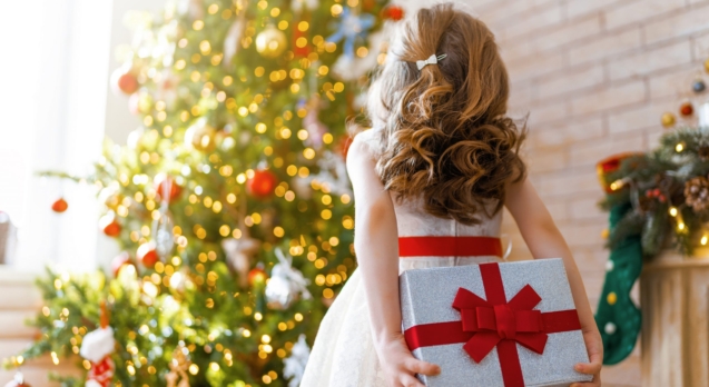 Merry Christmas and Happy Holidays! Cheerful cute child girl with gift. Kid is having fun near tree.