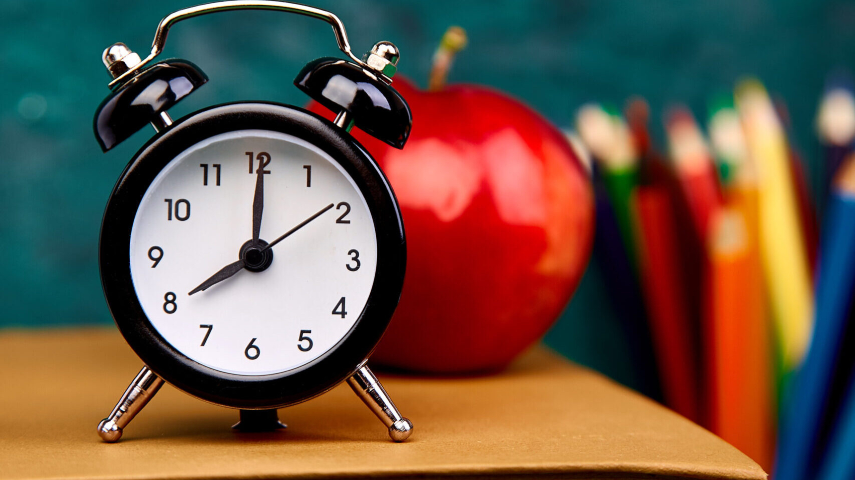 Back to school supplies. Books and red apple on green background. Still life with alarm clock. Copy space.