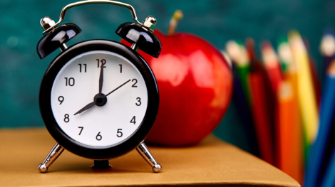 Back to school supplies. Books and red apple on green background. Still life with alarm clock. Copy space.