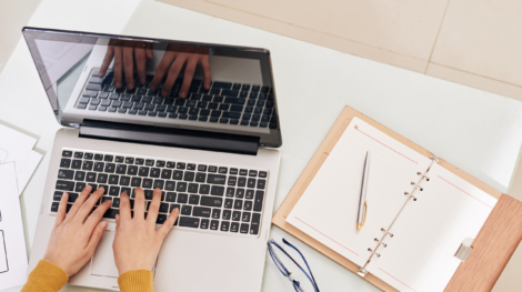 Hands of female back end developer working on laptop with her opened planner near by